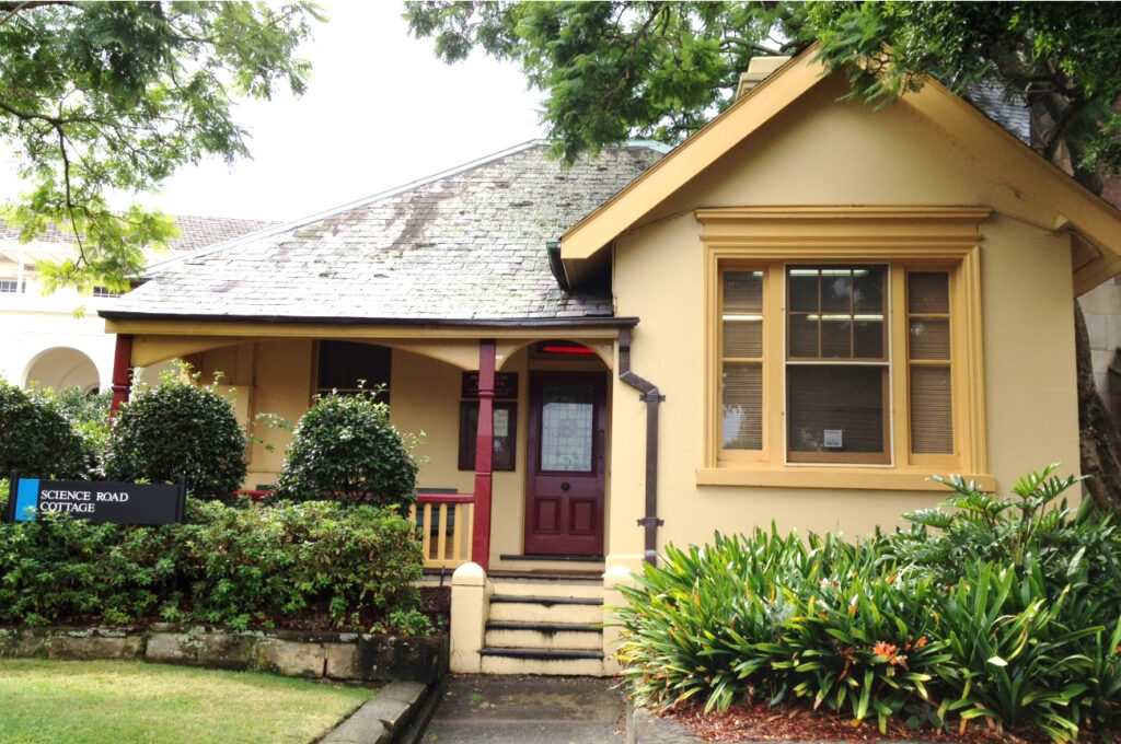 Science Road Cottage, a small yellow cottage with greenery in front